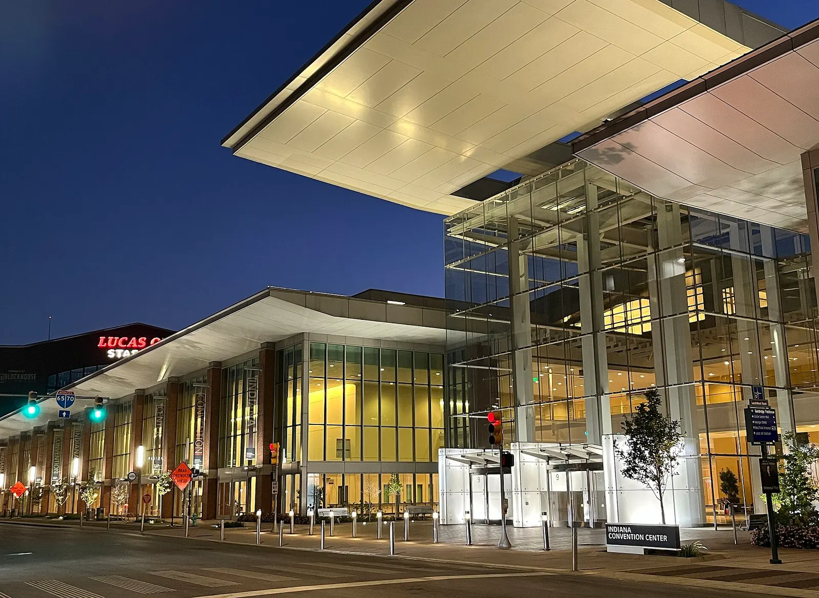 The glass Capitol Avenue entrance of the Indiana Convention Center at dusk, with Lucas Oil Stadium signage beyond