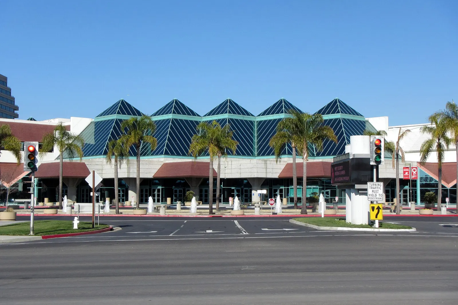 The pyramid-roofed glass entrance of the Santa Clara Convention Center behind palm trees and fountains